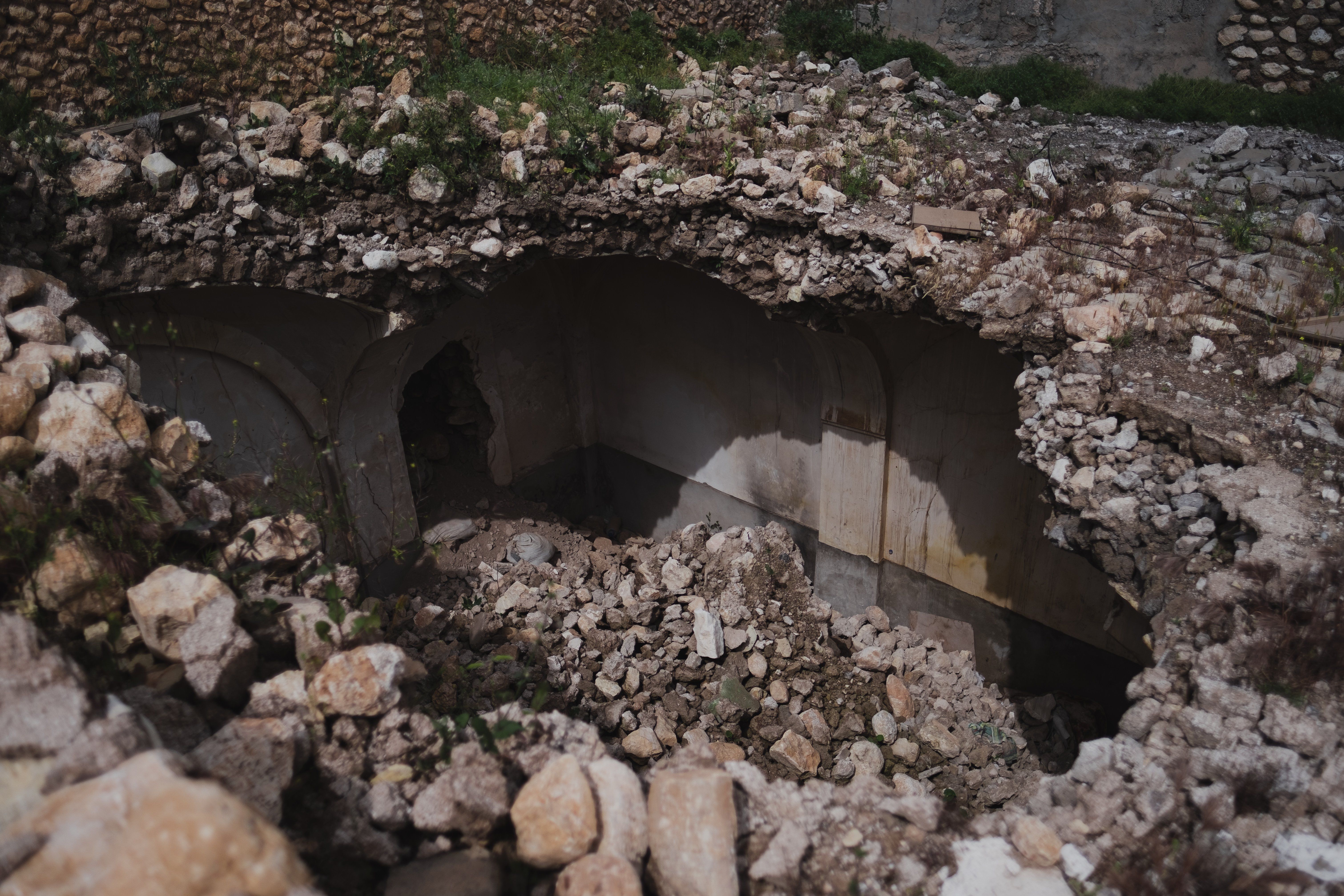 The image shows a collapsed bridge in the middle of a dirt field, surrounded by stones and grass....