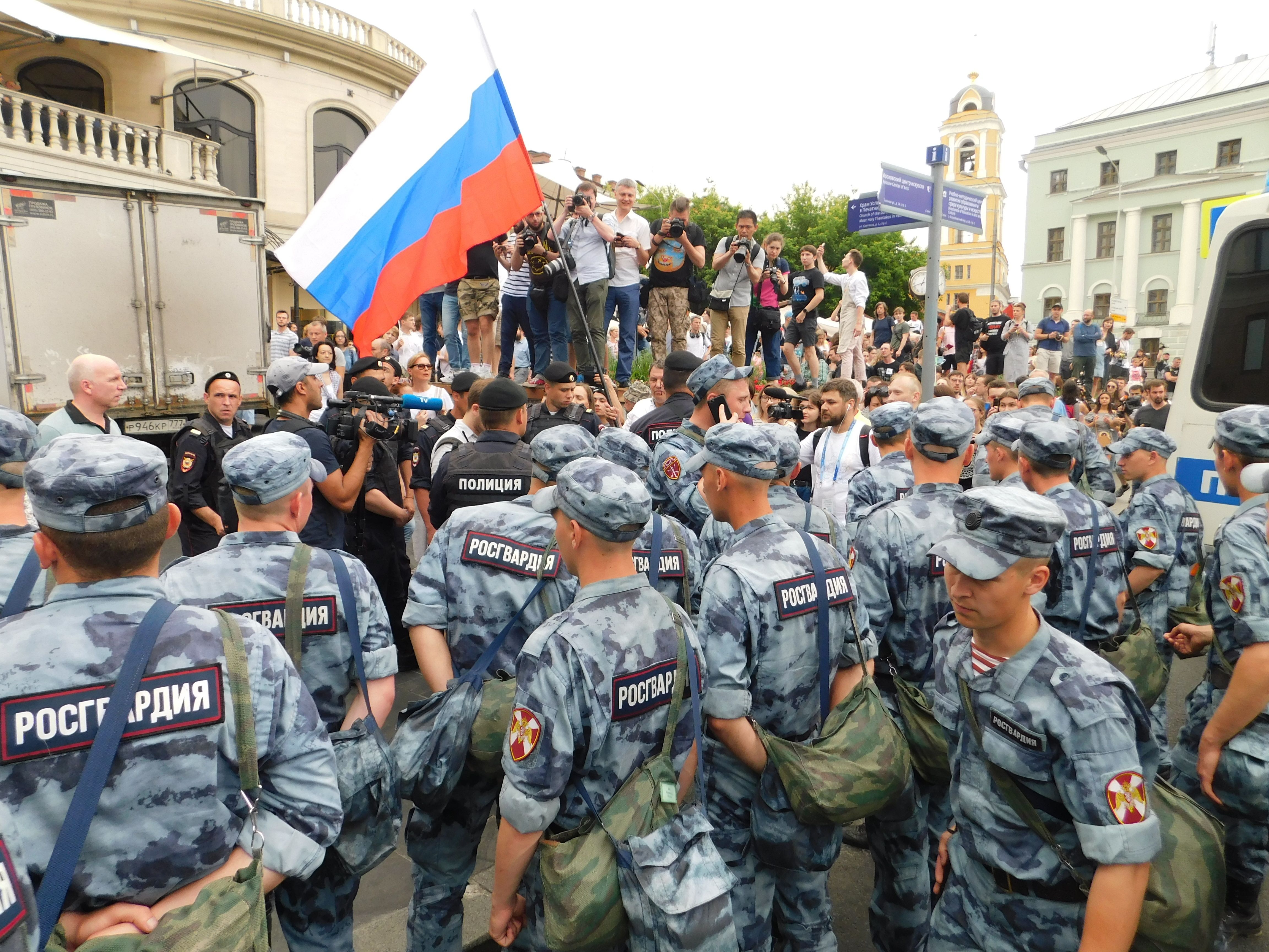 The image shows a group of Russian soldiers standing in front of a crowd of people, some of whom...