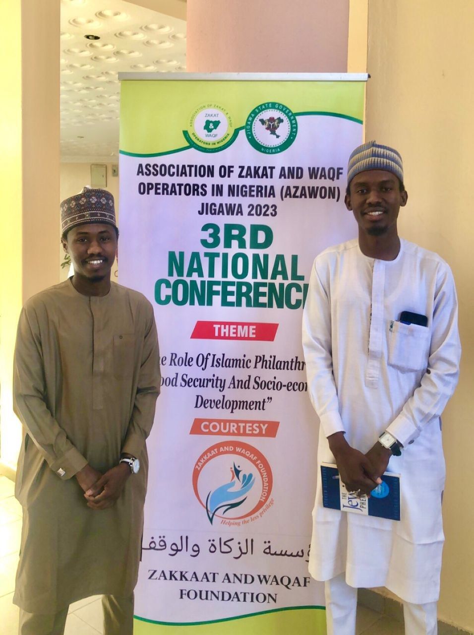 The image shows two men standing next to each other in front of a banner that reads "3rd National...