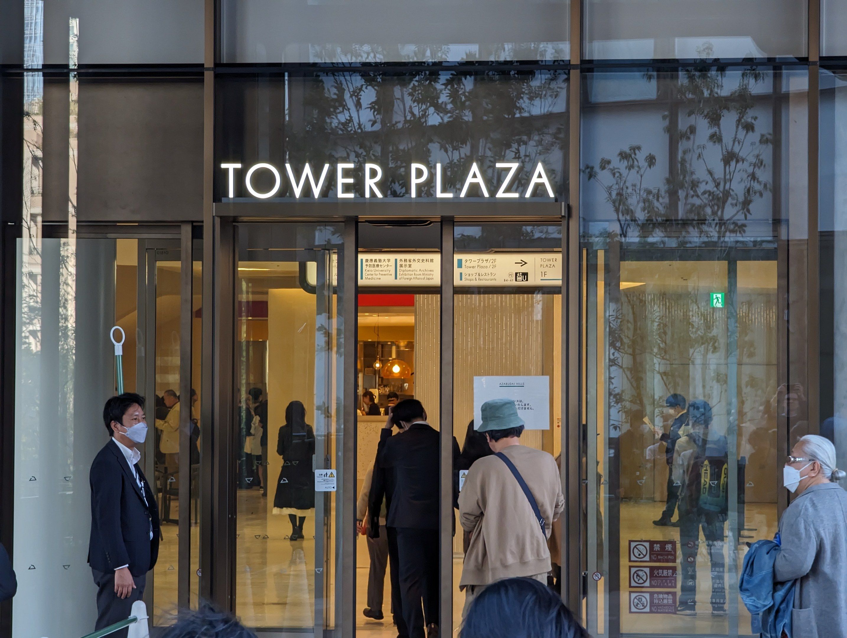 The image shows a group of people standing in front of a building with glass walls and doors. Some...