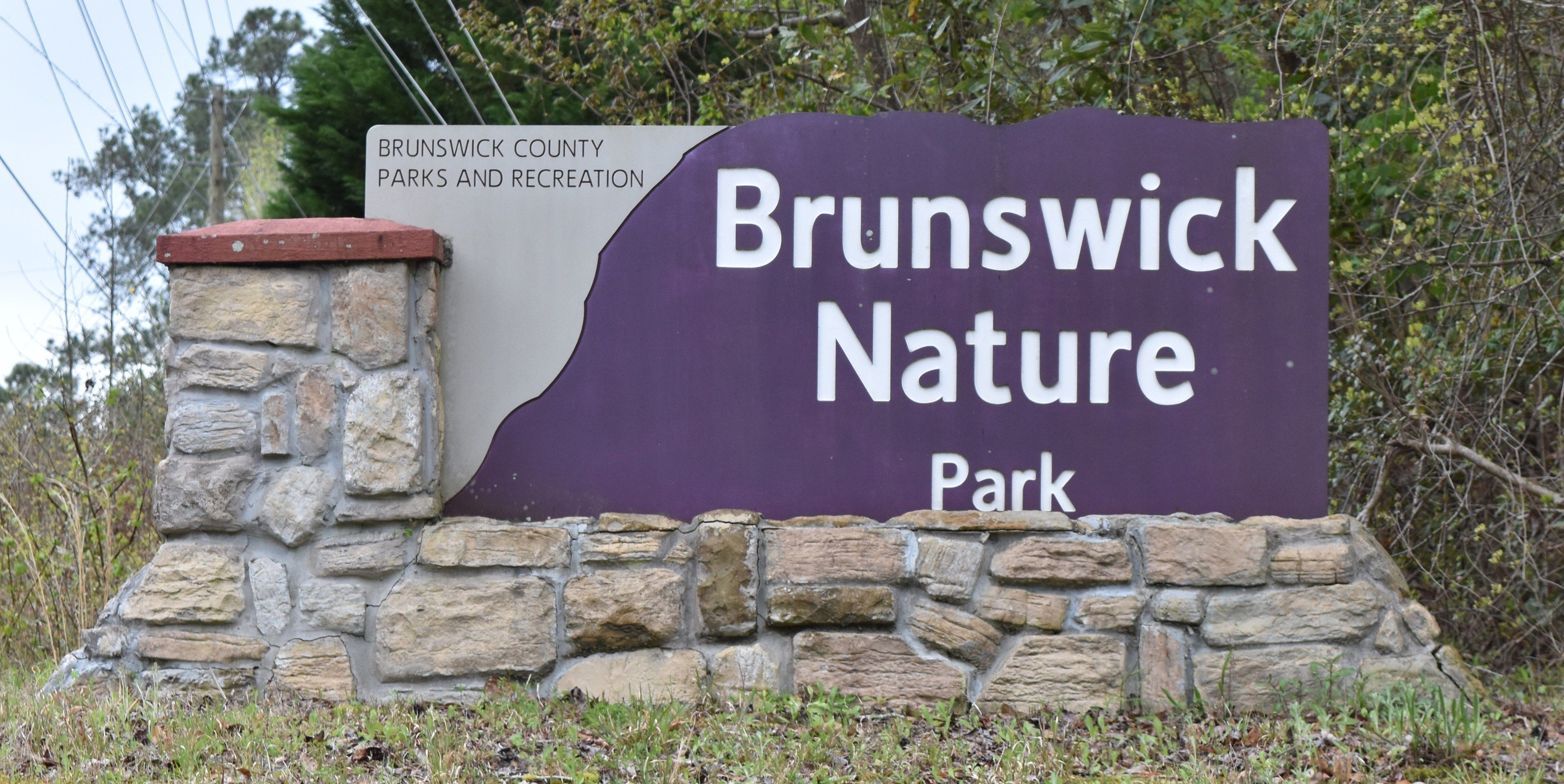 The image shows a name board on a stone wall with the words "Brunswick Nature Park" written on it,...