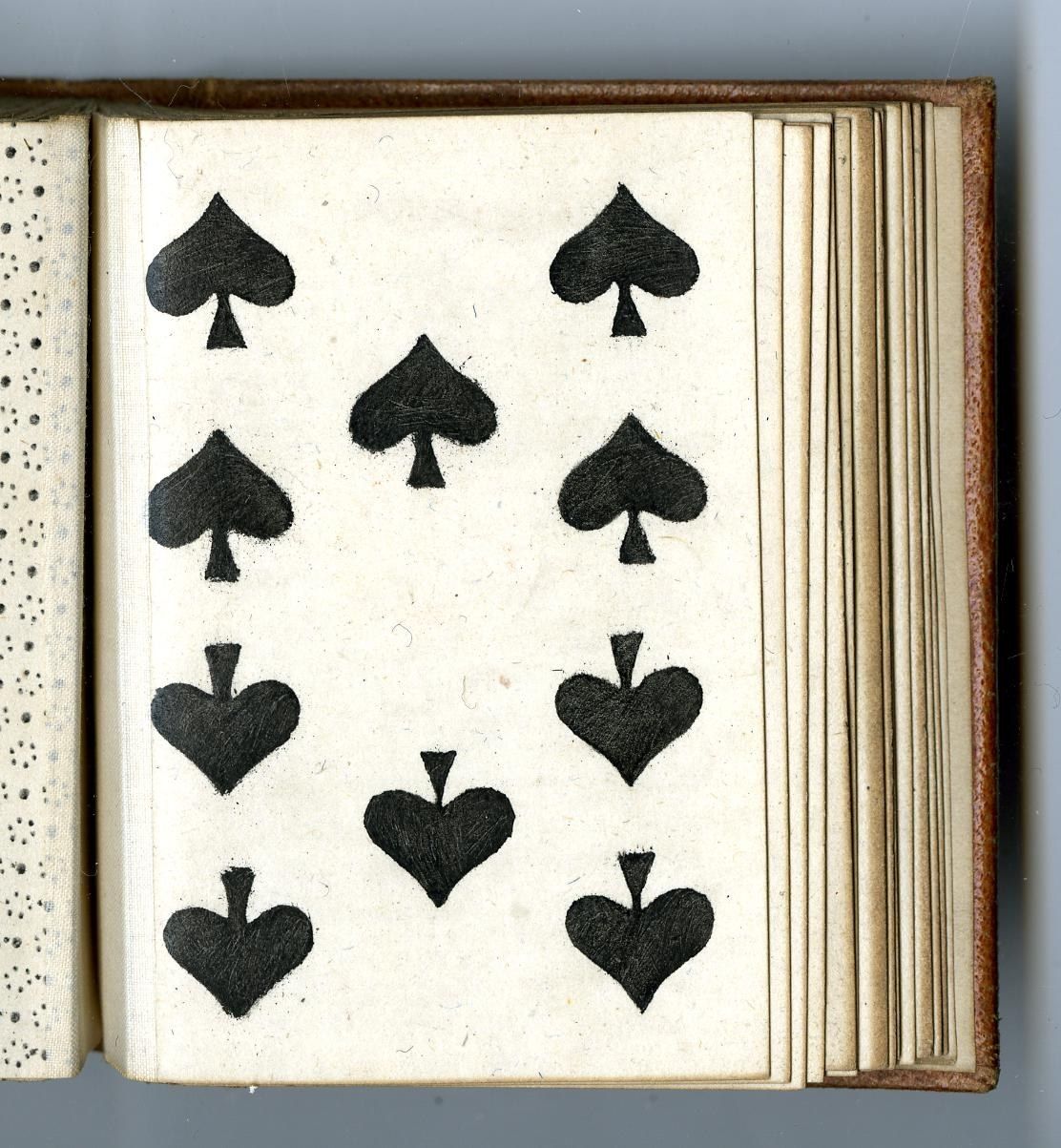 The image shows an open book with a black and white image of a deck of playing cards on it. The...
