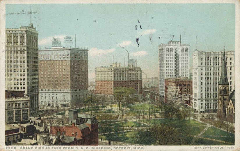 The image shows an old postcard of a city with tall buildings, trees, grass, and a sky with clouds...