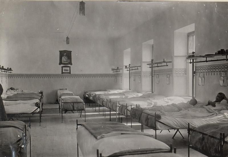 The image shows a black and white photo of a room filled with lots of beds, with a person lying on...