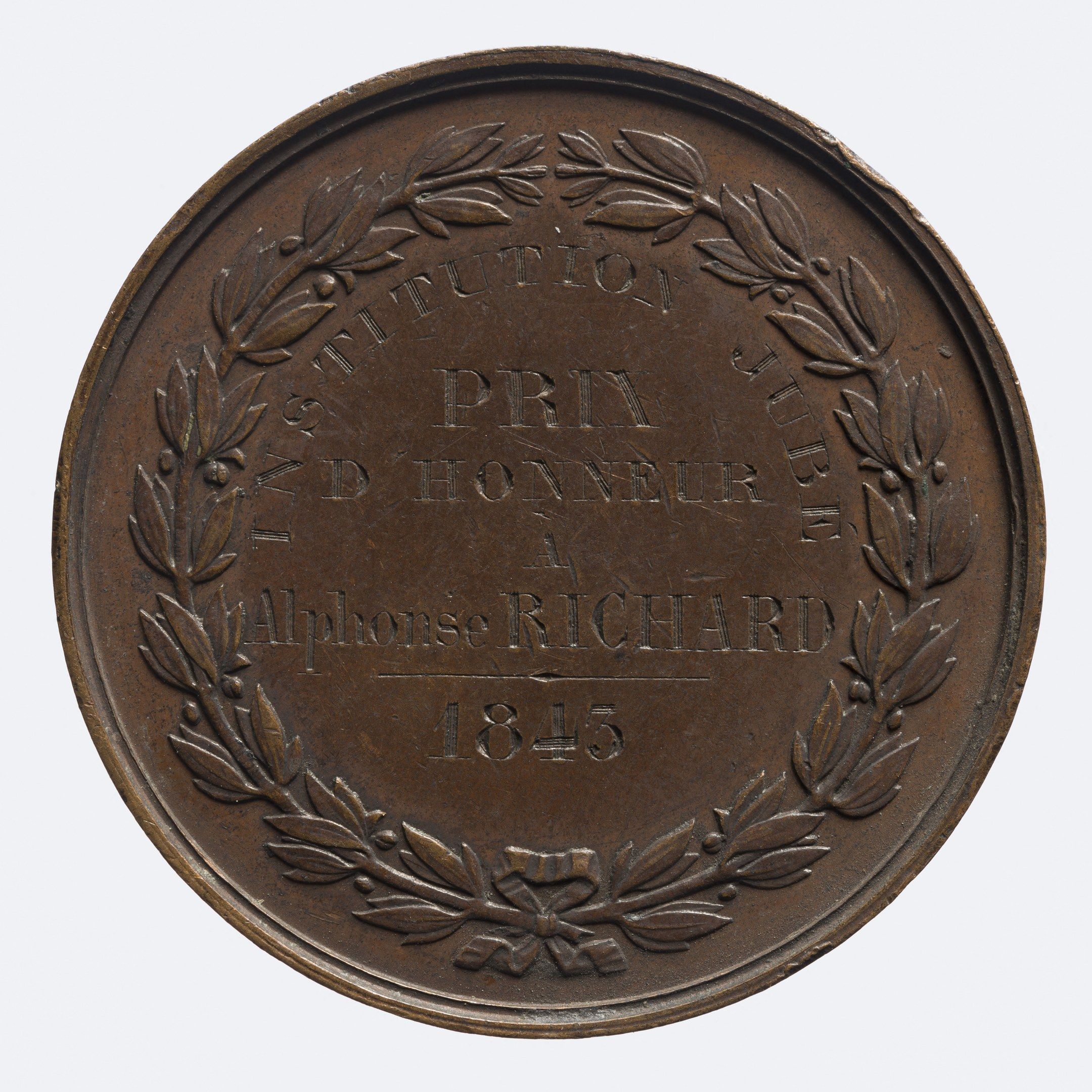 The image shows a bronze medal with a laurel wreath on it against a white background. The medal is...