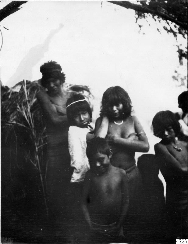 The image shows a black and white photo of a group of people standing next to each other in front...