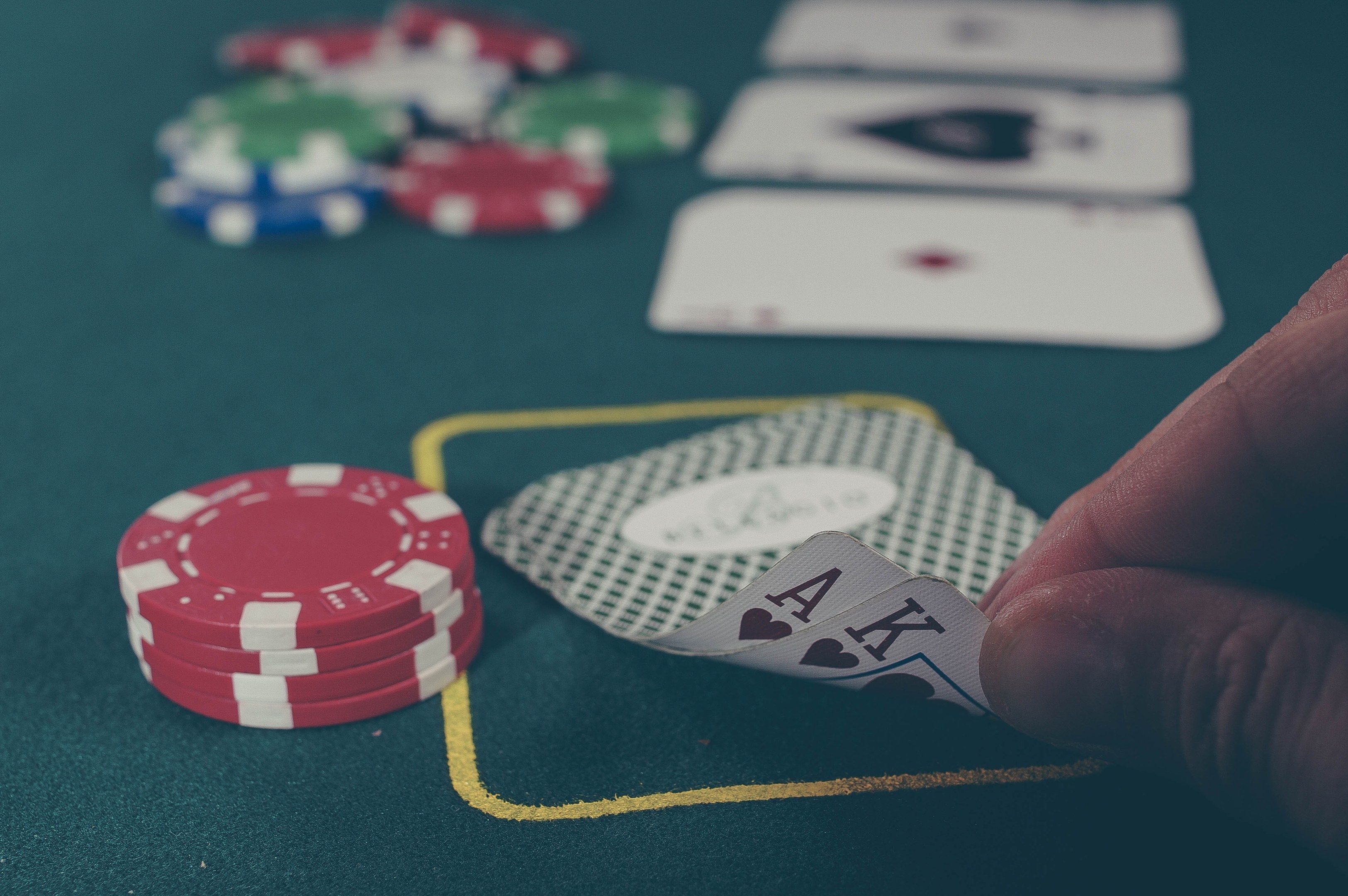 The image shows a hand holding a pair of aces on top of a green table, surrounded by red, blue, and...