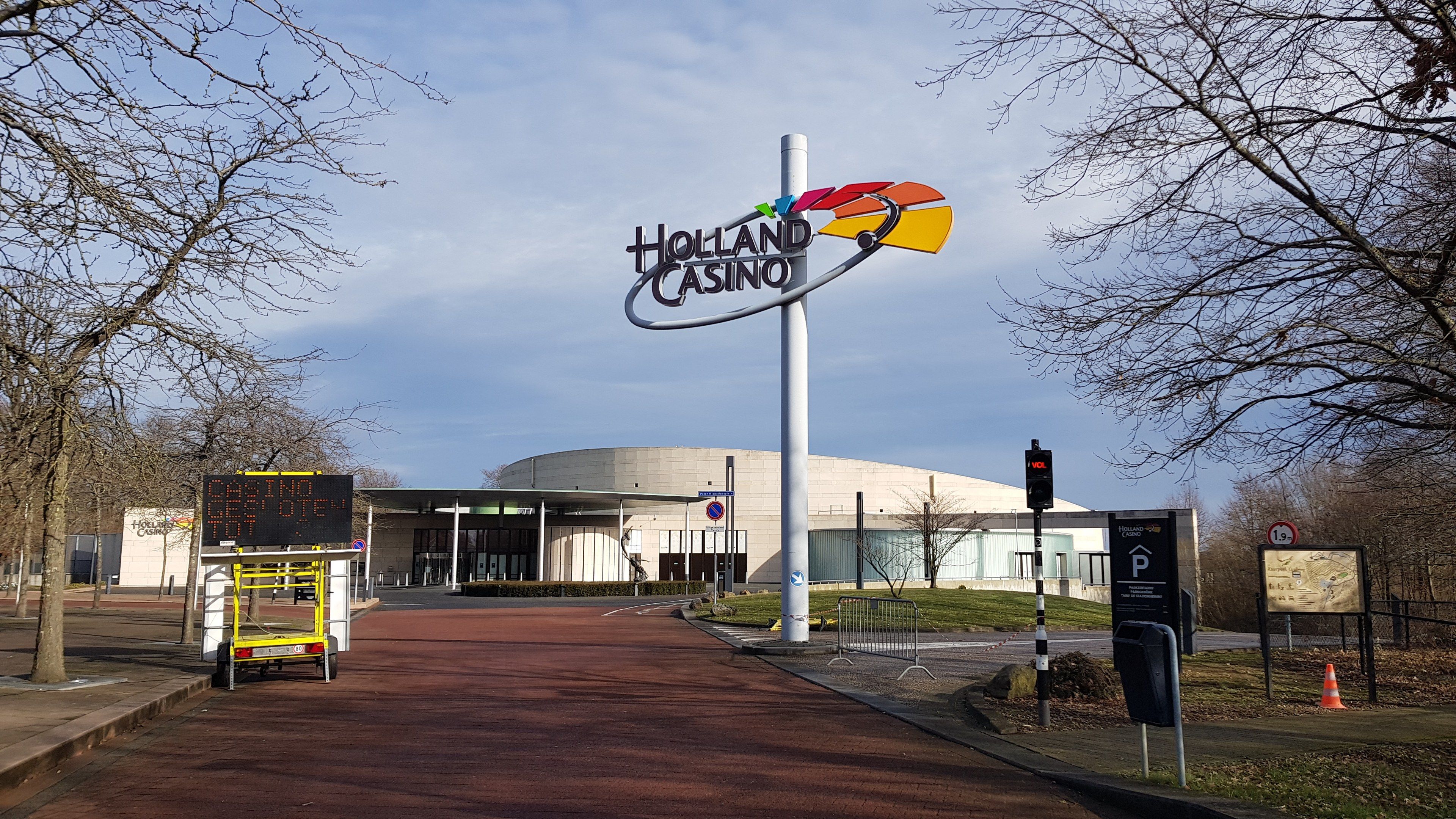 The image shows the Holland Casino in London, England, with a road in the foreground, grass on the...