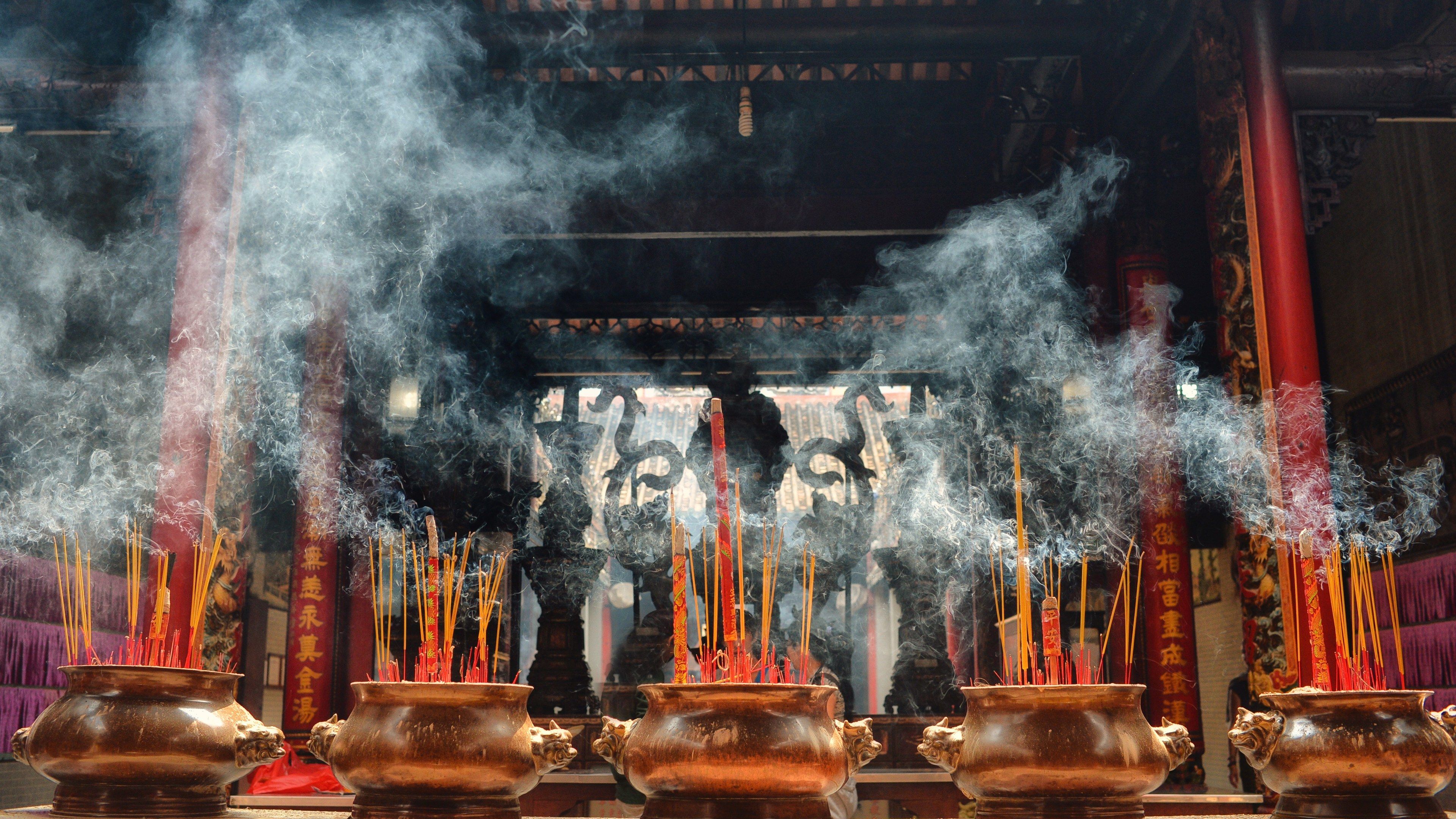 The image shows a group of incense sticks burning in a Buddhist temple, with smoke billowing out of...