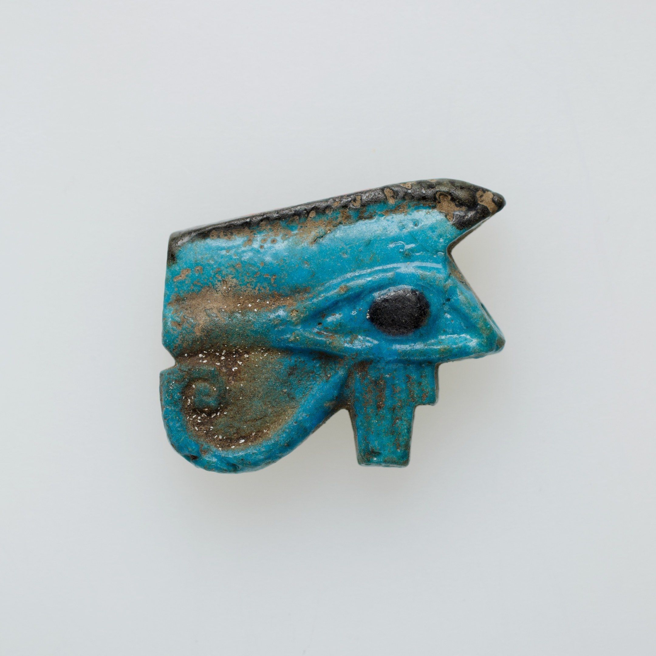 The image shows an ancient Egyptian faience amulet in the shape of an eye of Horus, which is blue...