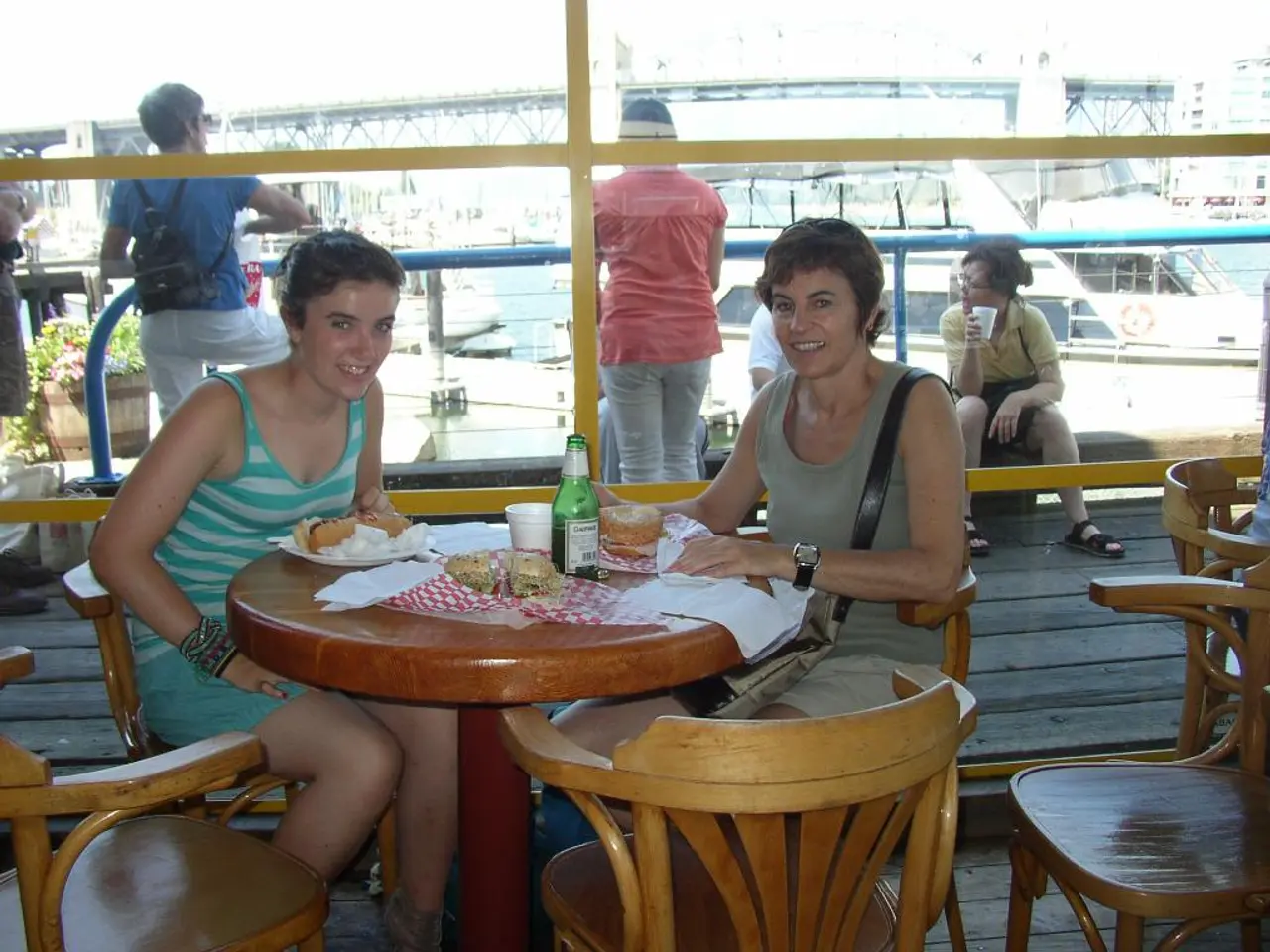 The picture is taken inside a ship it looks like a boat house there is a table and two women are...