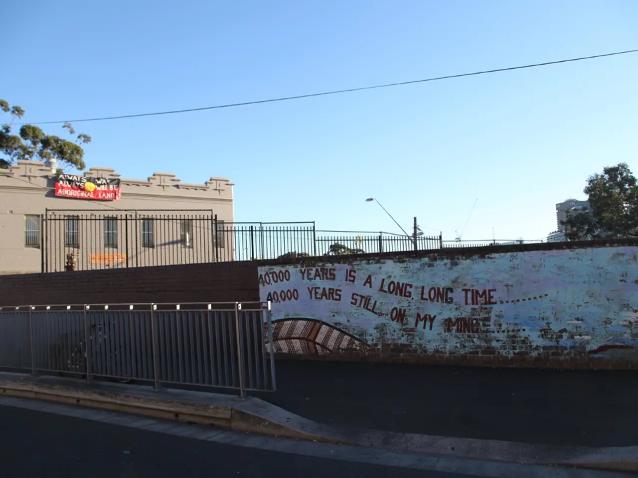 In the foreground of the picture there are road, railing, plant, wall, text and footpath. In the...