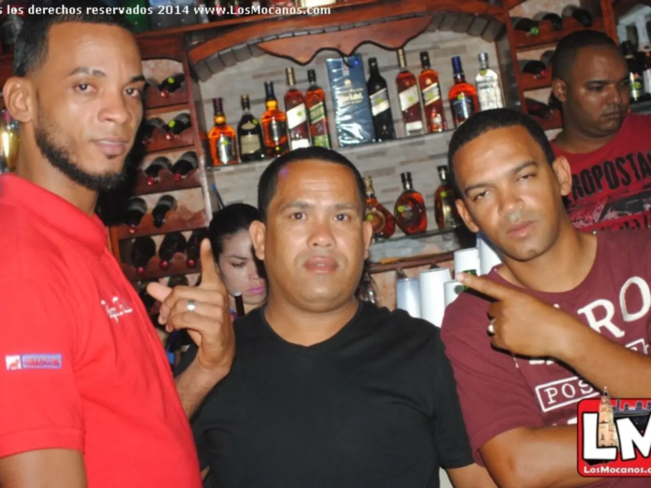 Here we can see a people. Background there is a rack filled with bottles. Top of the image there is...