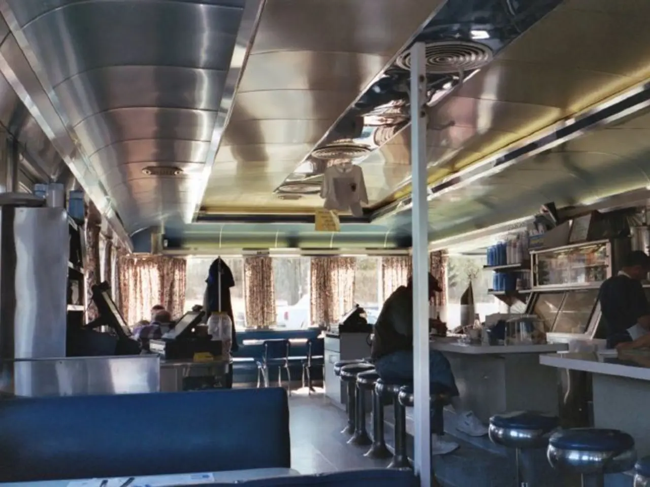 This picture shows a restaurant where people seated and we see two people standing and we see some...