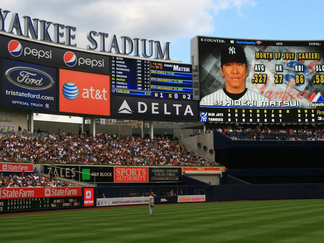 In the picture we can see a stadium with a grass surface and a person standing on it and behind him...