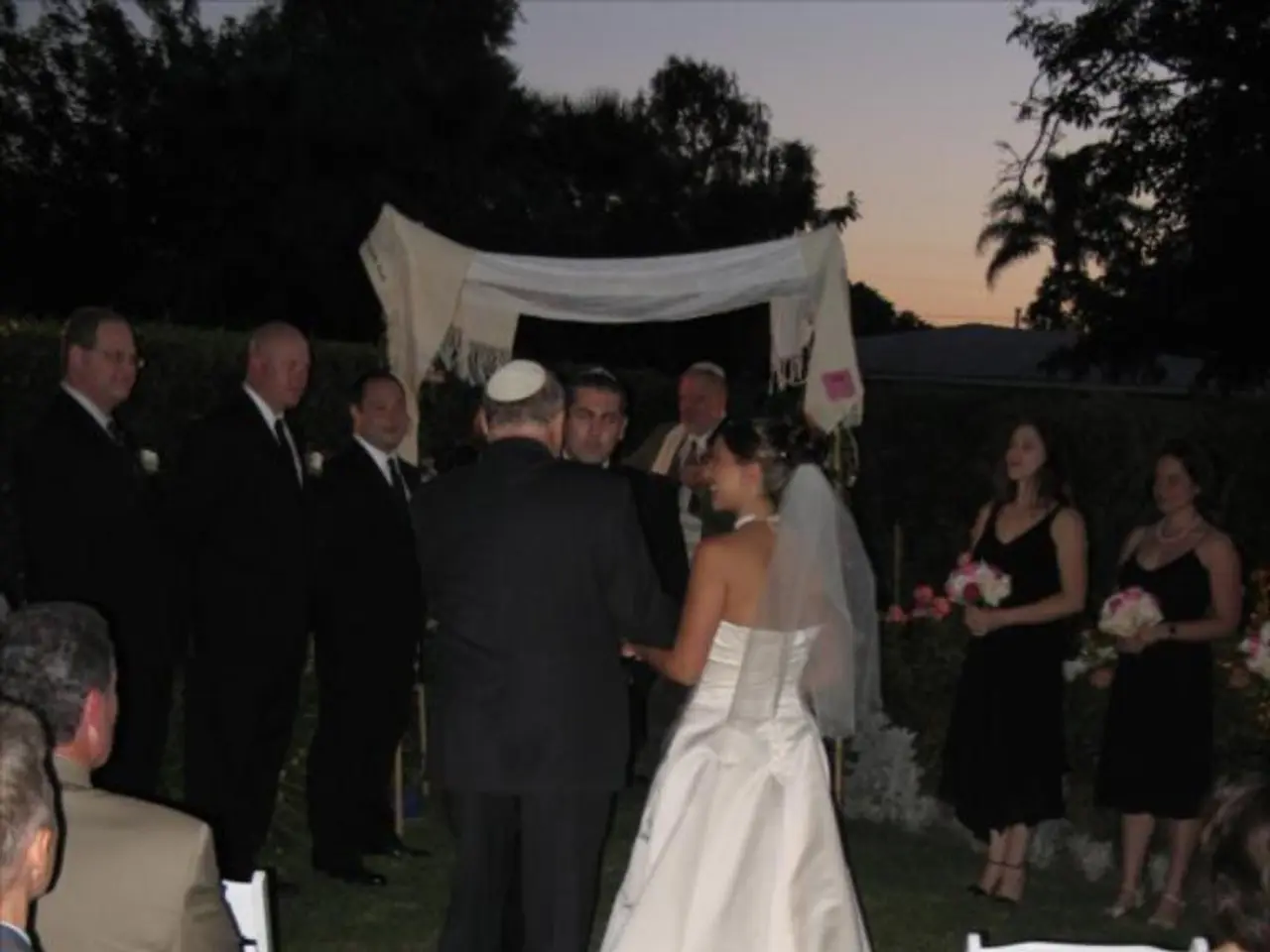 Here we can see a group of people standing, attending a wedding and the women on the right side are...