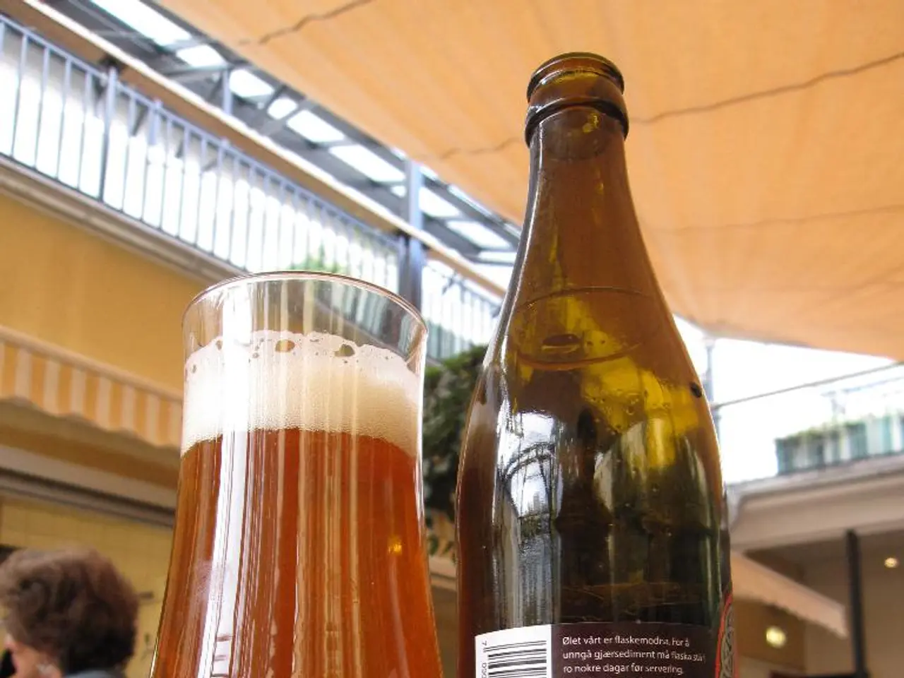 In this image there is a glass of wine , wine bottle kept in a table, and in back ground there are...