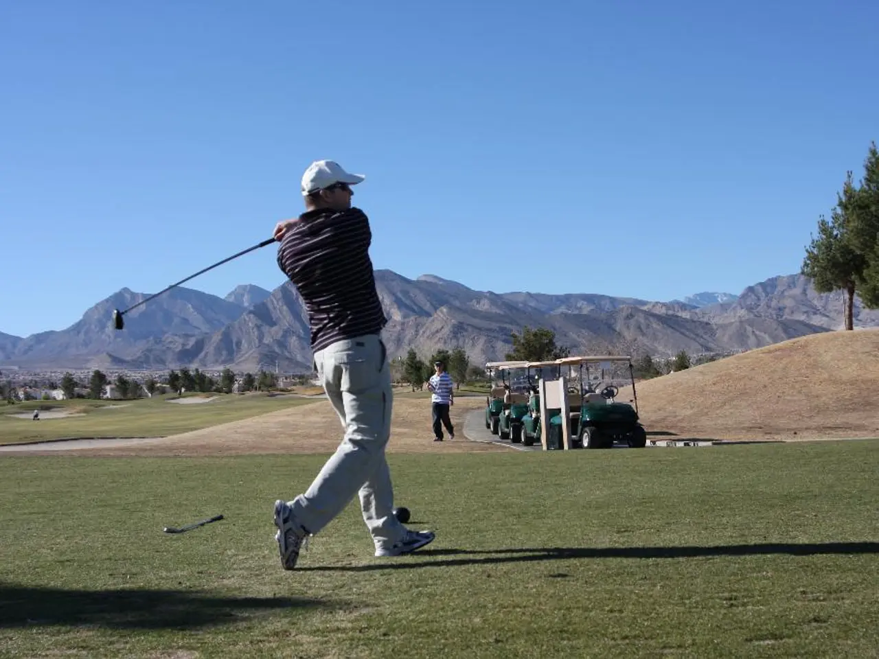 In this image in the center there is a man playing. In the background there is a man walking and...