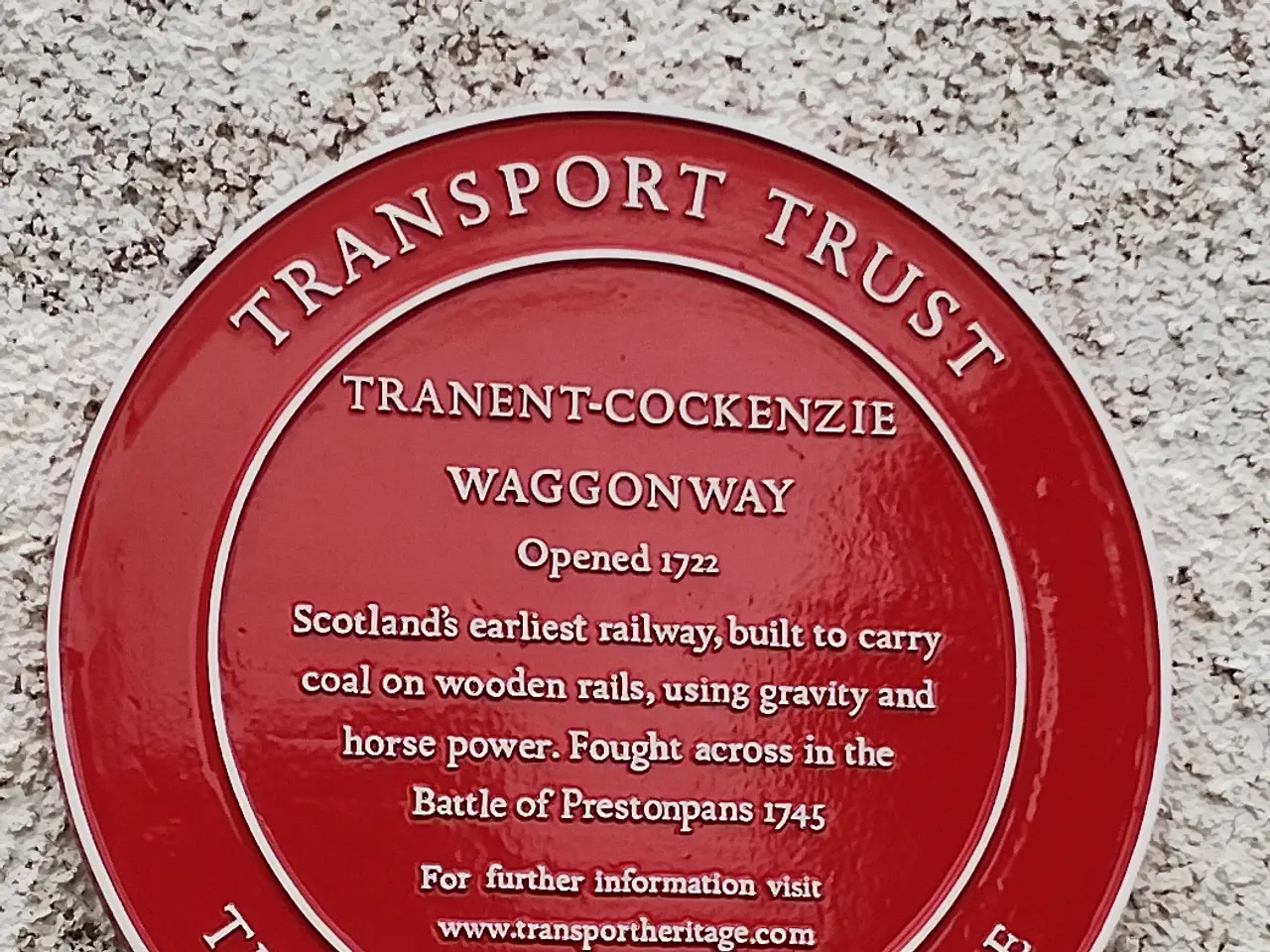 The image shows a red plaque on the side of a building that reads "Transport Trust". The plaque is...