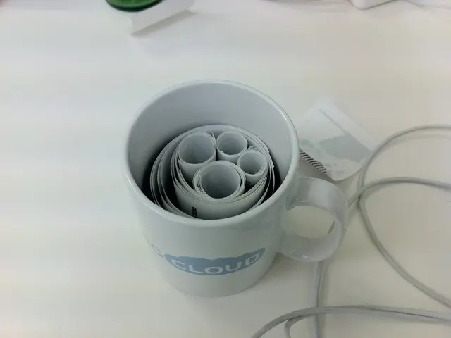 In the image there is a coffee cup with paper roll inside it on a table, beside it there is a wire...