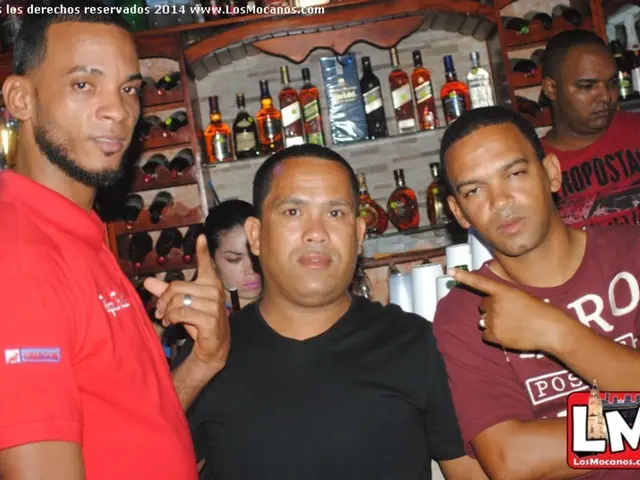 Here we can see a people. Background there is a rack filled with bottles. Top of the image there is...