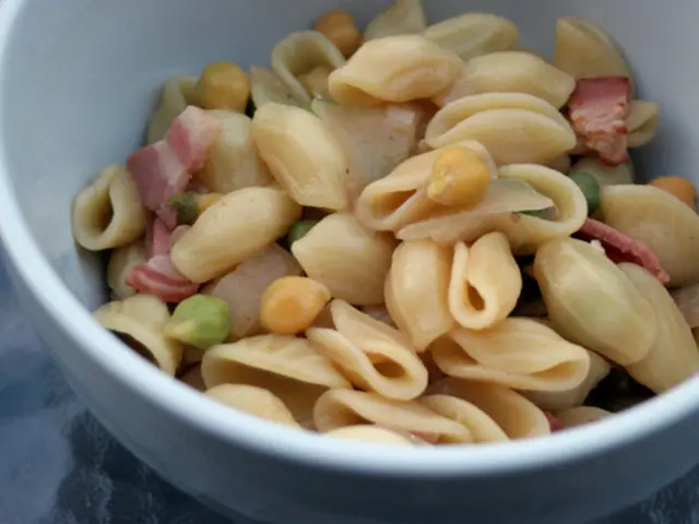 In this image we can see a bowl containing pasta placed on the surface.