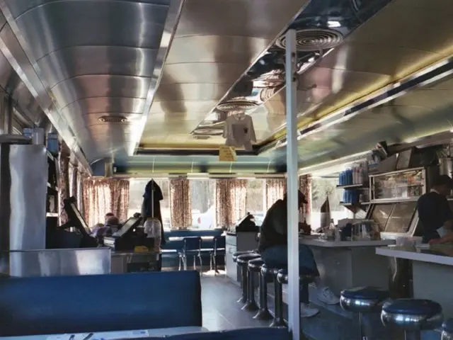 This picture shows a restaurant where people seated and we see two people standing and we see some...