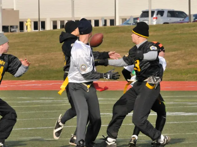 In this image we can see a few people playing rugby in the ground, there are some buildings, poles,...