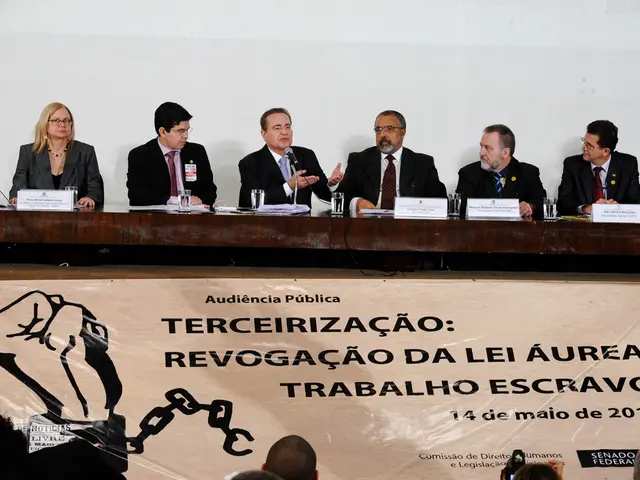 In this image we can see four men and one woman is sitting. They are wearing suits. In front of...