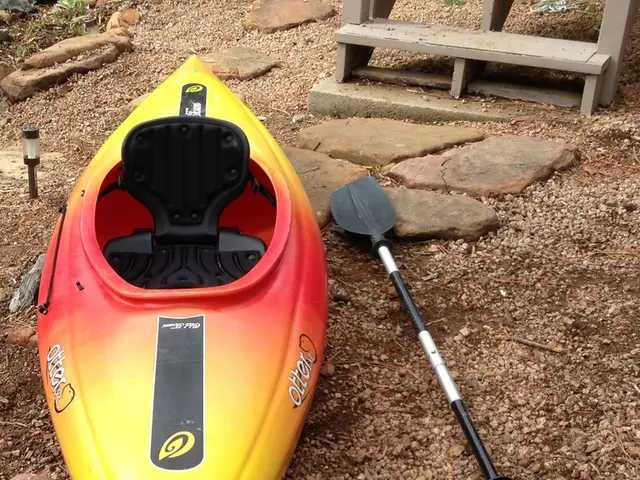 In this picture a boat and a stick is placed on the rocks and behind that there is a bench.