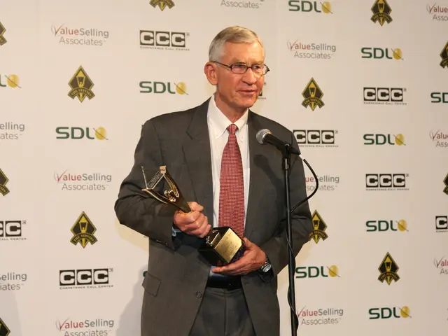 In this image we can see a man standing in front of a mike and holding a trophy with his hands. He...