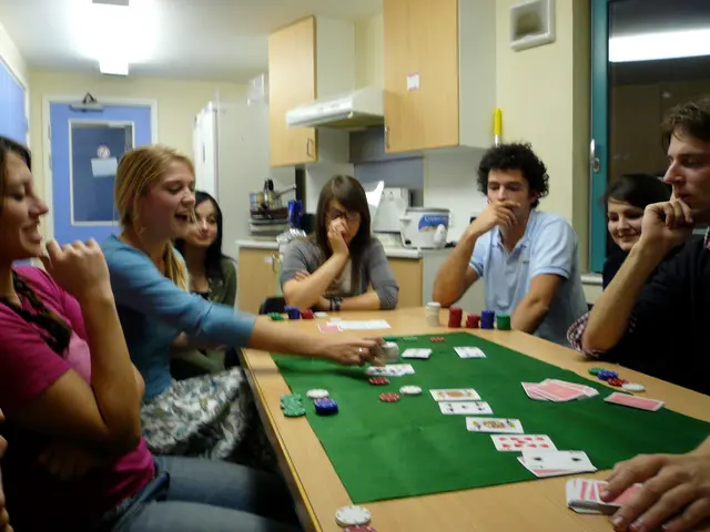 There are many people sitting over a table. They are playing cards. There is a green mat kept on...