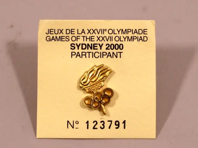 The image shows a gold pin with the words "Jeu de la XXVII Olympiade Games of the Olympic Sydney...