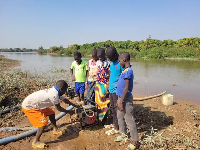 The image shows a group of children standing next to each other near a body of water, with one of...