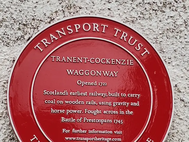 The image shows a red plaque on the side of a building that reads "Transport Trust". The plaque is...