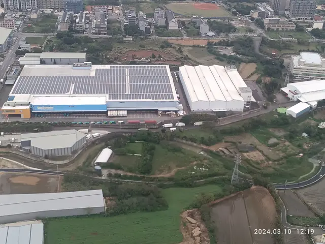 The image shows an aerial view of a large industrial area with buildings, trees, grass, roads,...