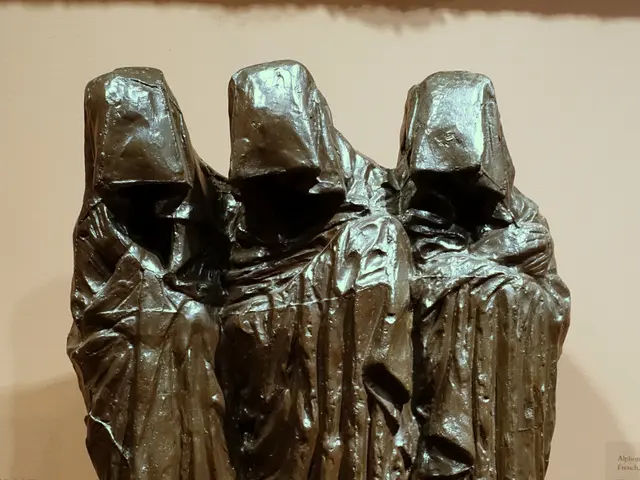 The image shows a bronze sculpture of three women in robes on display in a museum. The sculpture is...
