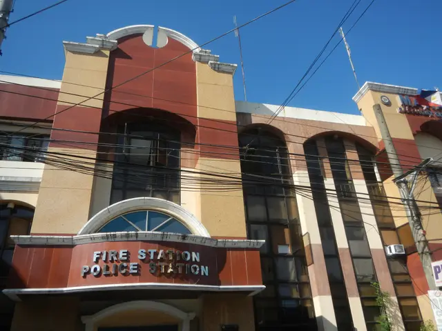 The image shows a fire station with a sign on the side of it, surrounded by buildings, electric...