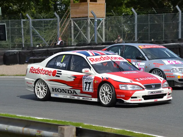 The image shows two cars racing on a race track with a metal fence in the background. The cars have...