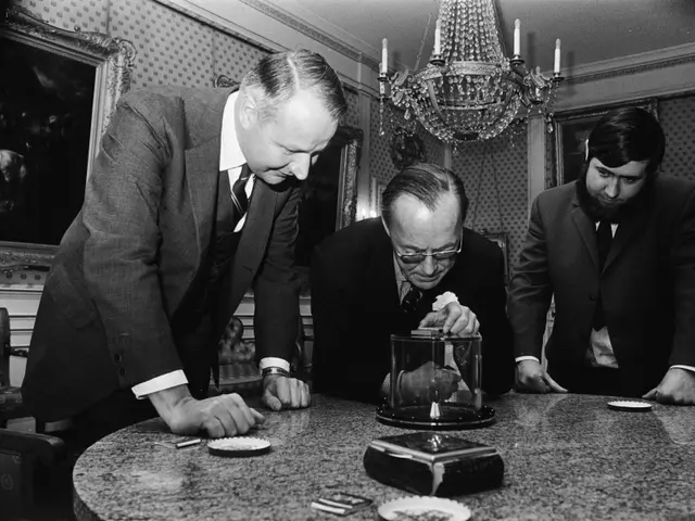 The image shows three men wearing blazers, ties, and shirts, sitting around a table with coins and...
