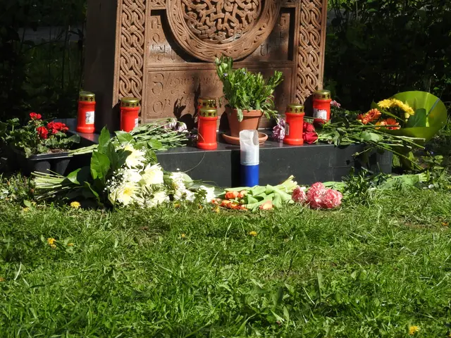 The image shows a memorial in the middle of a grassy area with a variety of flowers and candles...