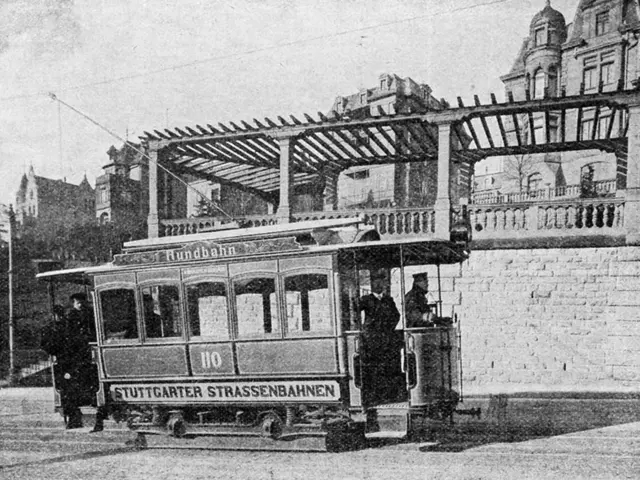 The image shows an old black and white photo of a tram on the street, with a few people inside. In...