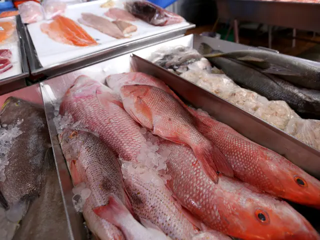 The image shows a bustling fish market with a variety of fresh fish on display in trays, surrounded...