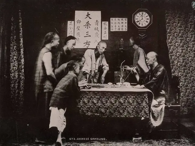 The image shows a group of people sitting around a table in a room, playing Chinese gambling. On...