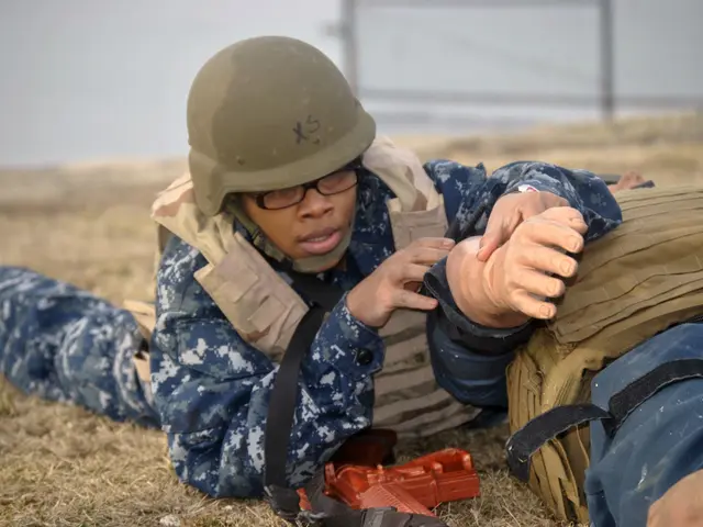 The image shows a man in a military uniform laying on the ground next to another man, both of them...
