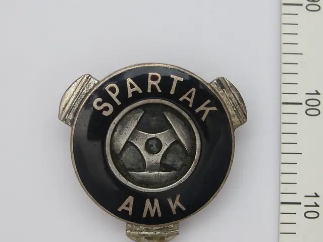 The image shows a spartak amk lapel pin on a white surface with a scale beside it. The pin is black...