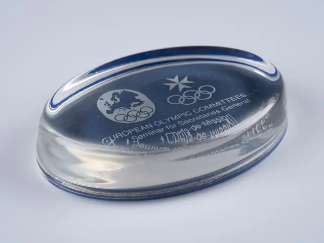 The image shows a clear glass award with a blue and white logo on it, sitting on a white surface....