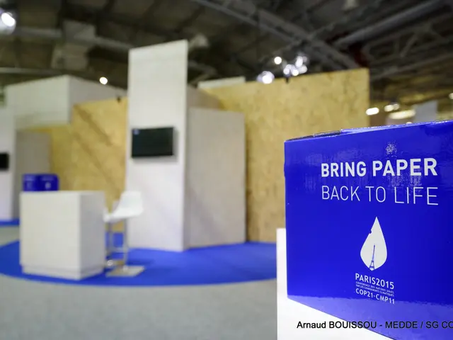 The image shows a trade show booth with a blue and white sign that reads "Bring Paper Back to Life"...