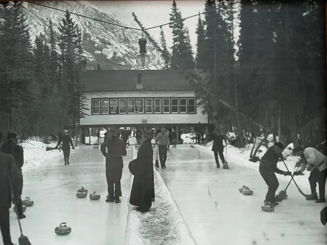 The image shows a group of people playing curling on an ice rink surrounded by trees and a building...