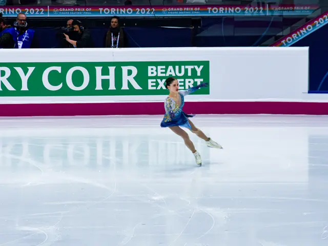 The image shows a woman in a blue dress gracefully gliding across an ice rink, surrounded by a...